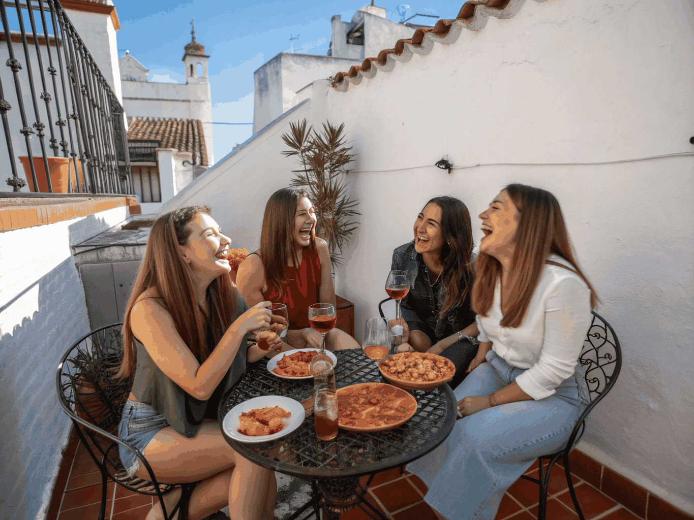 Grupo sorridente de mulheres à volta de uma mesa de esplanada a partilhar café e conversas